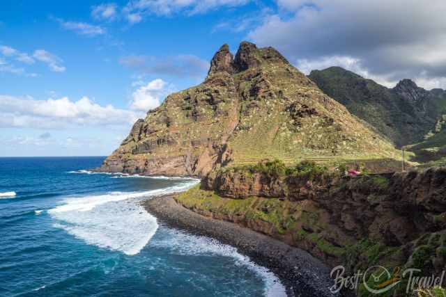 Rugged volcanic cliffs rising sharply from the shoreline at Punta del Hidalgo, with waves crashing onto a dark pebble beach.