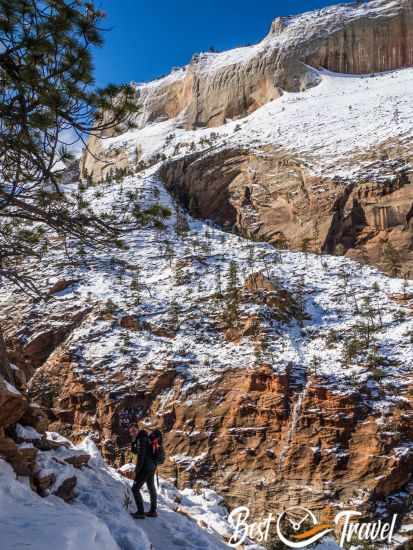 A hiker at higher elevation with snow capped mountains in Zion.