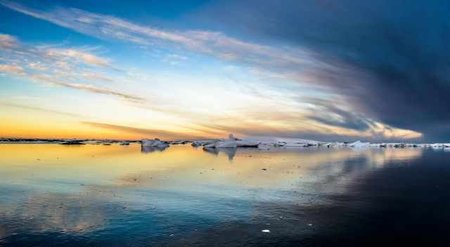 Magical atmosphere with blue, yellow, and orange lights on the icebergs at sunset