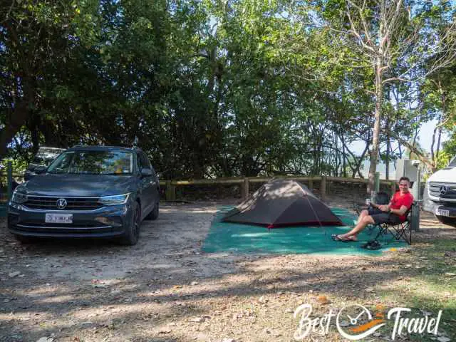 A man in front of a tent next to the beach.