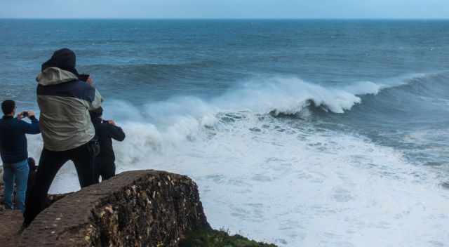 People in winter clothes on the lighthouse watching big waves.