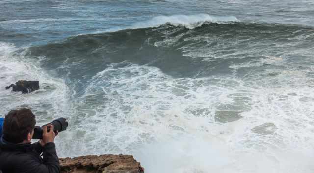 A man with zoom camera is taking a picture of a big wave.