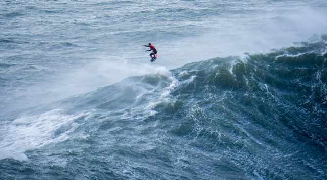 Surfer jumping on top of a monster wave in Nazare