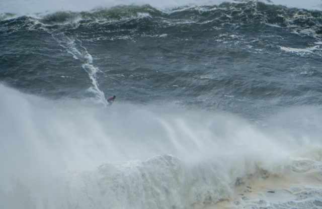 Surfer riding a massive wave and one on front of him is already crashing