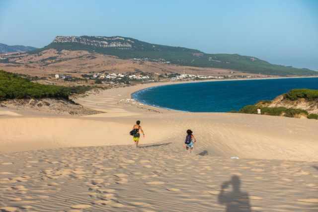 Two children running down the dunes direction sea.
