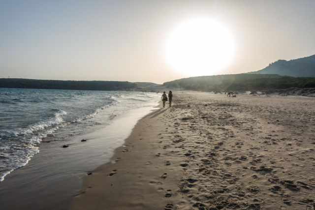 Two children walking along the beach shortly before sunset.