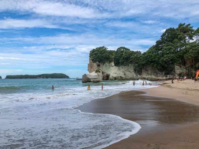 Cathedral Cove’s second beach in summer with visitors in the water and a lifeguard on the right near the cliffs.