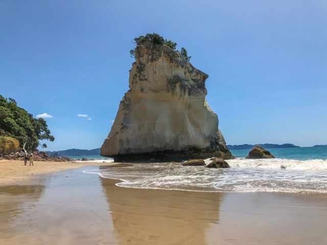 Te Hoho Rock at Cathedral Cove with visitors walking along the beach and cliffs covered in vegetation.
