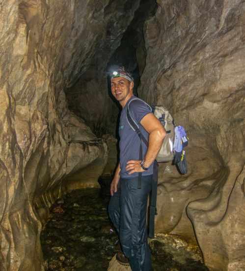 Man with headlamp in the cave and standing in water.