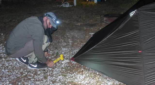 Essential mosquito net for the head - man pitching a tent in the night