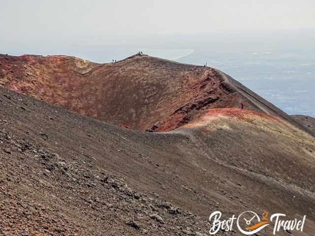 Visitors walking on an reddish orange crater rim on Etna.