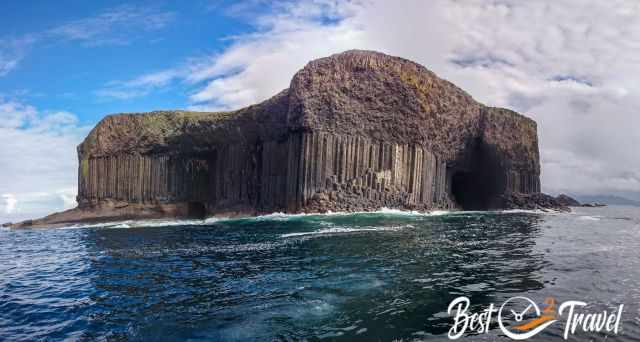 Basalt columns and the entrance of Fingal’s Cave rising above deep blue water on the Isle of Staffa in perfect weather.