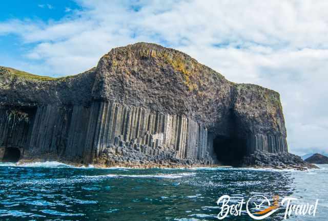 Basalt columns and cave openings on the Isle of Staffa rising above deep blue water, with rugged cliffs and patches of vegetation.