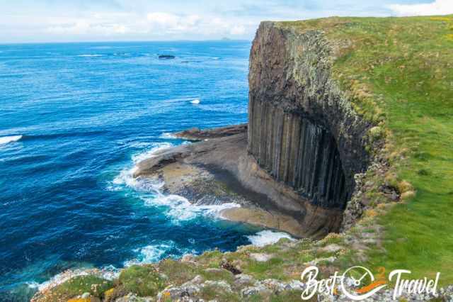 Top view of Fingal’s Cave on the Isle of Staffa, showing the dark cave entrance framed by steep basalt columns and rugged cliffs above the Atlantic.