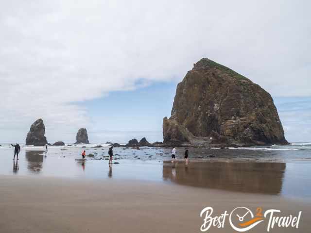visitors in front of Haystack Rock with a partly cloudy sky