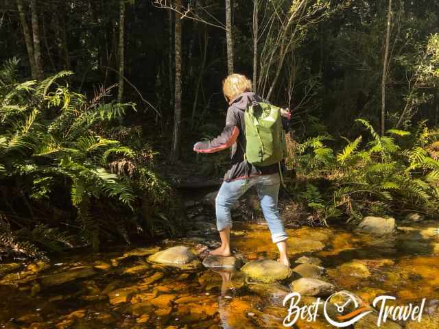 A female hiker crosses the creek barefoot
