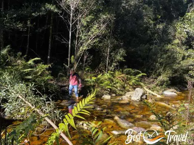 A female hiker crosses the creek barefoot