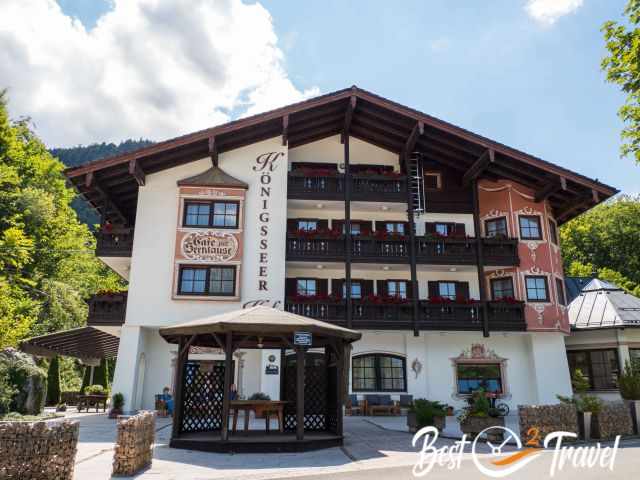 Traditional alpine guesthouse near Königssee with wooden balconies, red flowers and a small gazebo in front.