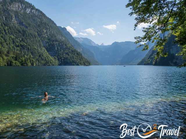 A man swimming below the Malerwinkel viewpoint with clear turquoise water and steep forested mountains in the background.
