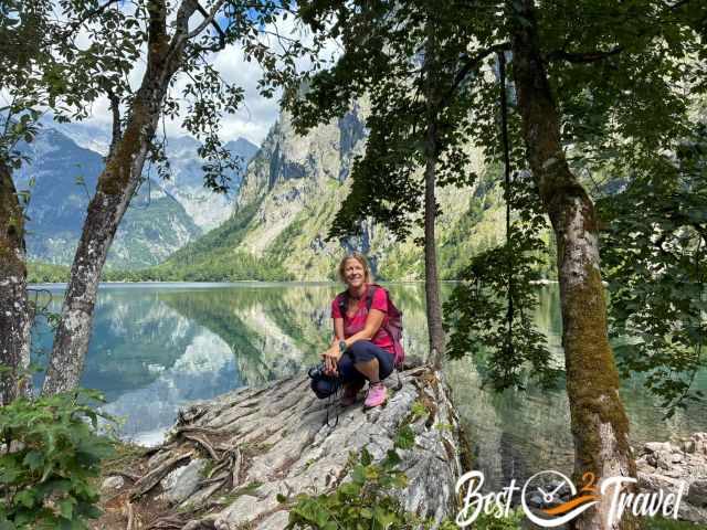 The author sitting on a rock at Oberersee, framed by trees with calm reflective lake water and steep mountains in the background.