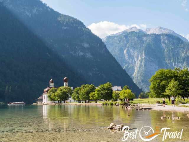Morning view from St. Bartholomä with the church, calm lake water and the steep mountain walls in the background.