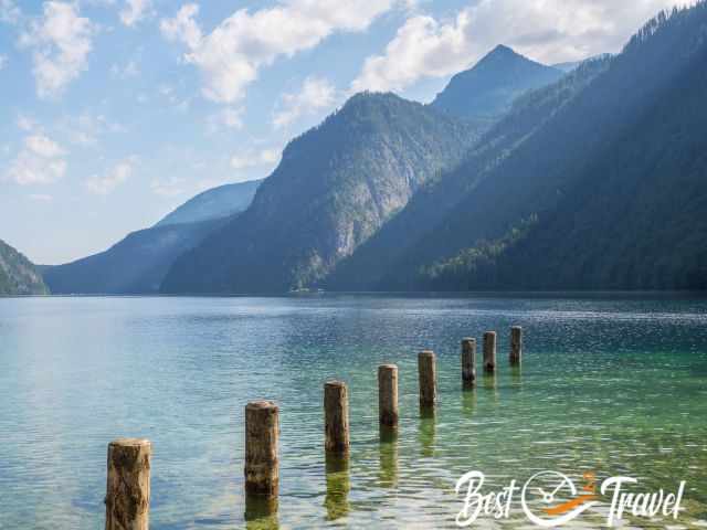 Morning view from St. Bartholomä with calm lake reflections and the mountains rising behind the wooden posts.
