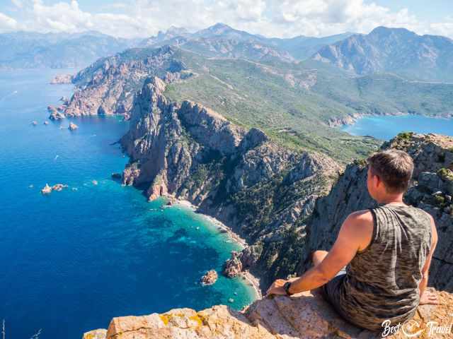 A hiker sits on a cliff overlooking the sea.