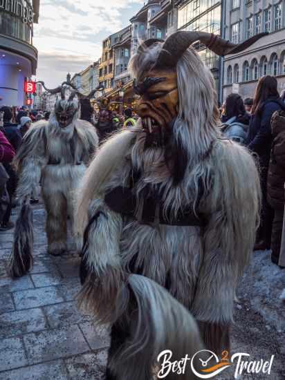 A costume with white fur, wooden mask and bent horns.