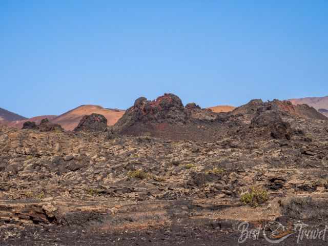  Reddish volcanic cones rising from the ground under a blue sky.