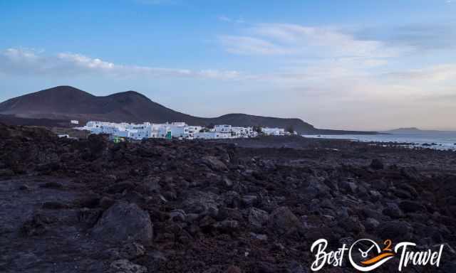 White houses rising above a black lava field next to the sea.