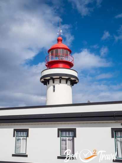 Red‑and‑white lighthouse at Ponta do Topo on São Jorge, standing against a blue sky.
