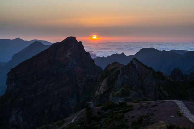 Sunset above the clouds at Pico do Arieiro, with rugged mountain ridges and a narrow trail leading through the dramatic high‑altitude landscape.
