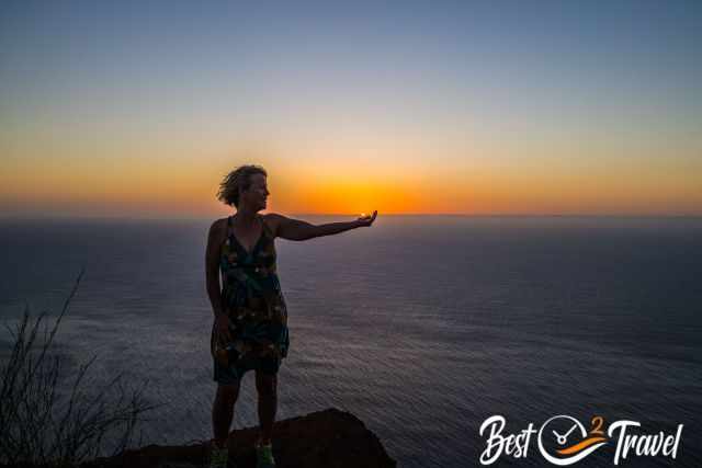 A woman holding the sun in her hand at sunset