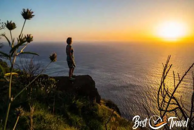 A woman on the edge of a cliff watching the sunset.