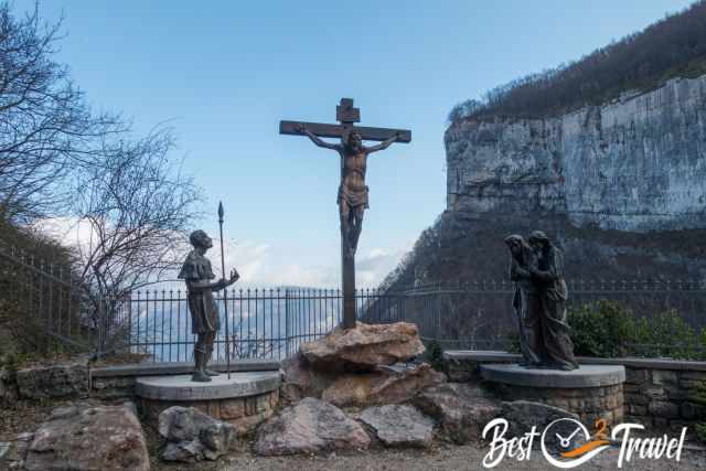 Bronze crucifixion group at the cloister near Madonna della Corona, with Jesus on the cross, a Roman soldier, and mourning figures set against the rocky mountain backdrop.