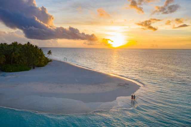 A couple watches the sunrise from the beach in Dhigurah