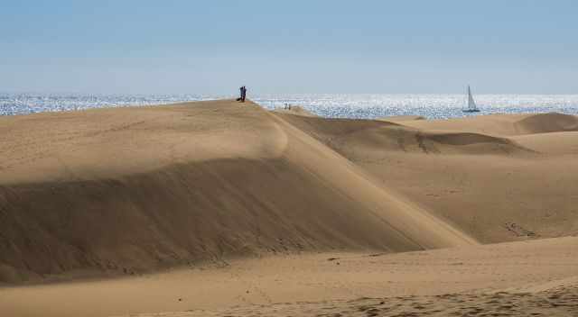 A couple on the dunes and a sailing boat in the back on the Atlantic Ocean