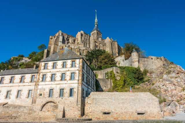 Mont‑Saint‑Michel viewed from the tidal flats, with the abbey rising above the stone walls under a clear sky.