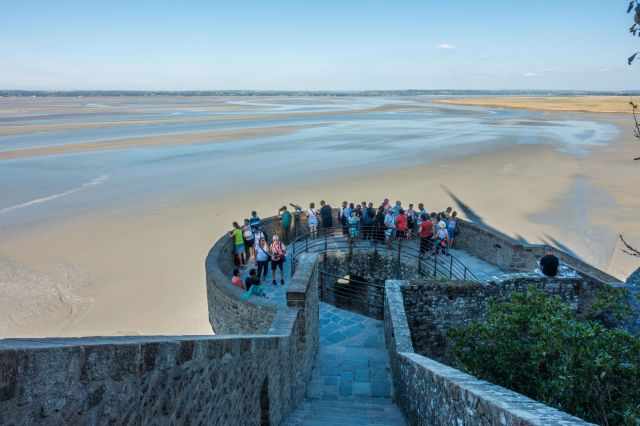 People standing on a stone viewpoint overlooking the wide tidal flats near Mont‑Saint‑Michel.