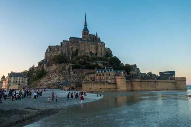 Mont‑Saint‑Michel at low tide with visitors walking across the tidal flats toward the abbey.