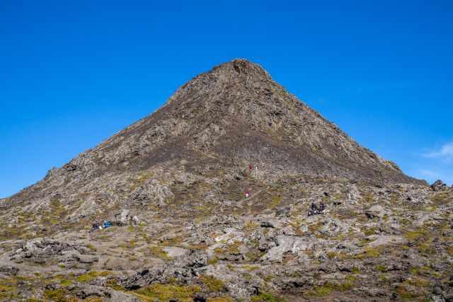 The crater of Pico Mountain and the cone of Pico with hikers on the rocky lava track.