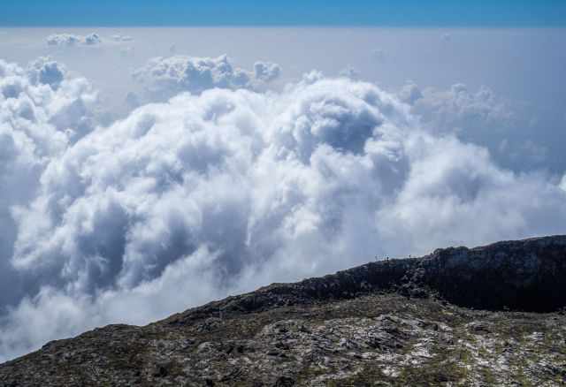 The crater of Pico mountain above a sea of clouds with hikers standing on the rim.