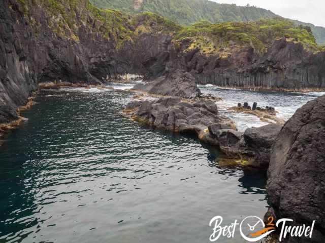 Volcanic rock formations at Poca Simão Dias with a sheltered natural pool on the left and the open sea on the right.