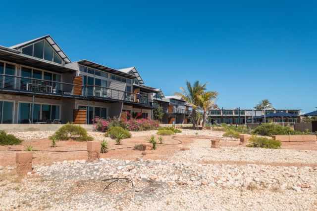 Modern Manta Ray Hotel in Exmouth with glass‑fronted rooms, balconies, and landscaped coastal surroundings under a clear blue sky.