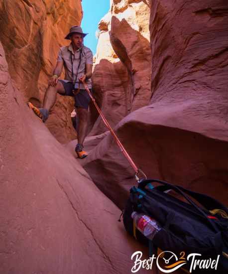 A hiker pulls up his backpack by a rope.