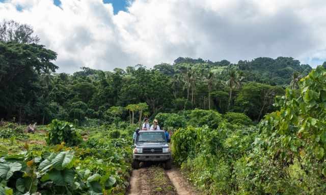 A jeep on a rough muddy road with people standing in the trunk.