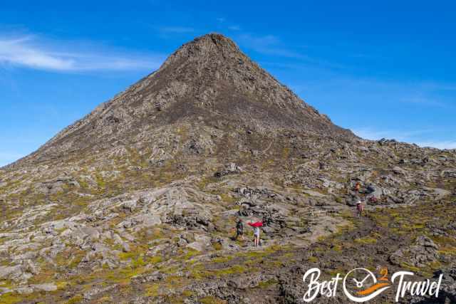 Hikers climbing the steep volcanic cone of Pico on rugged, rocky terrain under a clear blue sky.