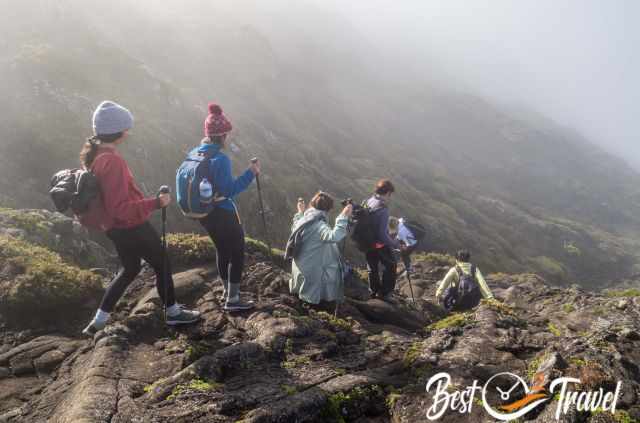 Group of hikers descending through misty, rocky terrain on Pico, surrounded by lush green slopes.