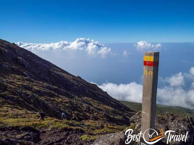 Trail marker 30 on Pico’s upper slope with hikers climbing above a thick cloud layer toward the summit.