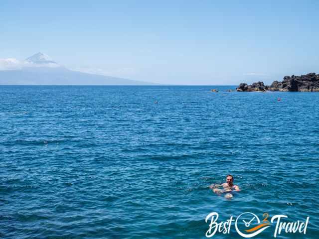 A man swimming in the sea on a calm day with Pico in the distance.